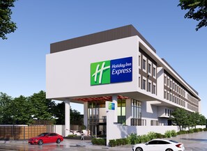 A Holiday Inn Express building with a prominent green and blue logo, a covered entrance, and a parking lot with cars. - Holiday Inn Express Bengaluru Bommasandra (Anekal)