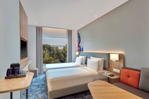 A hotel room with two beds, a desk, a chair, a TV, and a window with a view of trees and buildings. - Holiday Inn Express Bengaluru Bommasandra (Anekal)