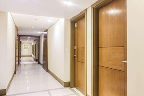 A hotel corridor with wooden doors, a tiled floor, and a long hallway. - PRS at One Palm Tree Villa Near Airport (Pasay)