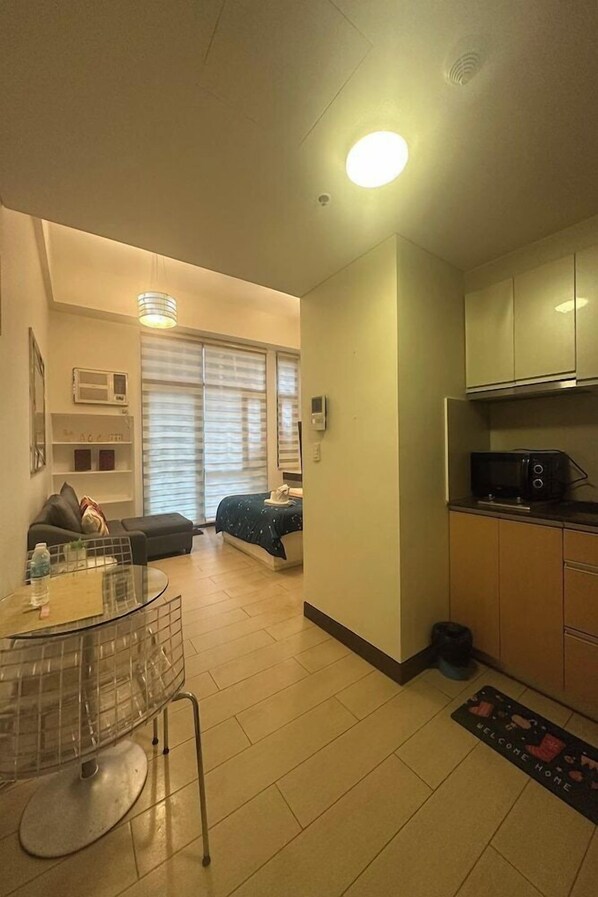 A compact living space with a kitchenette, a dining area with a glass table, a sofa, and a bed. - PRS at One Palm Tree Villa Near Airport (Pasay)
