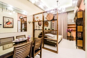 A compact hotel room with a dining area, a bed with a wooden headboard, and a decorative partition with cultural artifacts. - PRS at One Palm Tree Villa Near Airport (Pasay)