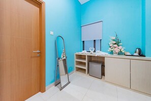 A room with a wooden door, a mirror, a whiteboard, a shelf with items, a trash bin, and a cabinet. - Sans Hotel Alexander Bandung (Bandung)