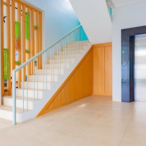A modern staircase with wooden steps and a glass railing, leading to a landing with a blue wall and a door. - Sans Hotel Alexander Bandung (Bandung)