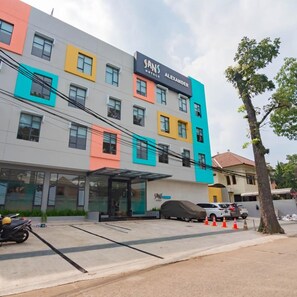 A multi-story hotel with a colorful facade, a covered entrance, and a parking area with a covered vehicle. - Sans Hotel Alexander Bandung (Bandung)