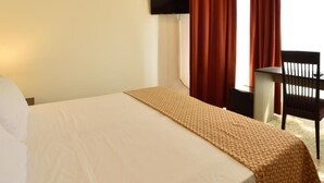 Una habitación de hotel con cama, escritorio, silla y televisor montado en la pared.