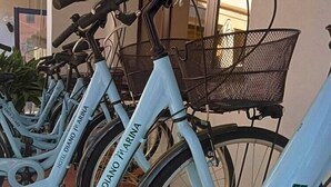 Una hilera de bicicletas con la marca 'HOTEL DIANO MARINA', estacionadas en un espacio al aire libre con suelo de baldosas y una canasta de metal en una de ellas.