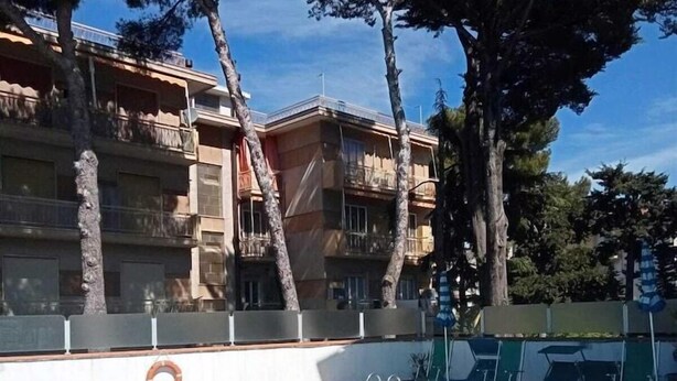 Una piscina con agua azul cristalina, rodeada de árboles y un edificio con balcones.