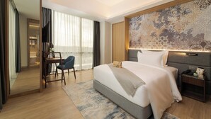Habitación de hotel con una cama grande, un escritorio, una silla, una mesita de noche y un amplio ventanal con cortinas.