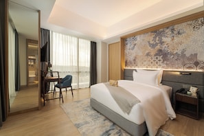 A hotel room with a large bed, a desk, a chair, a nightstand, and a large window with curtains. - Oakwood Hotel and Apartments Grand Batam (Batam)
