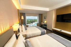 A hotel room with two beds, a TV, a desk, a chair, a lamp, and a view of the outdoors. - Gokulam Grand Hotel Thiruvananthapuram (Thiruvananthapuram)