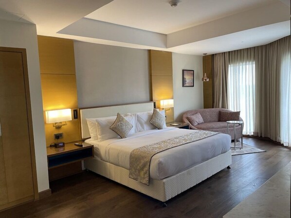 A hotel room with a large bed, a sofa, a desk, and a window with curtains. - Gokulam Grand Hotel Thiruvananthapuram (Thiruvananthapuram)