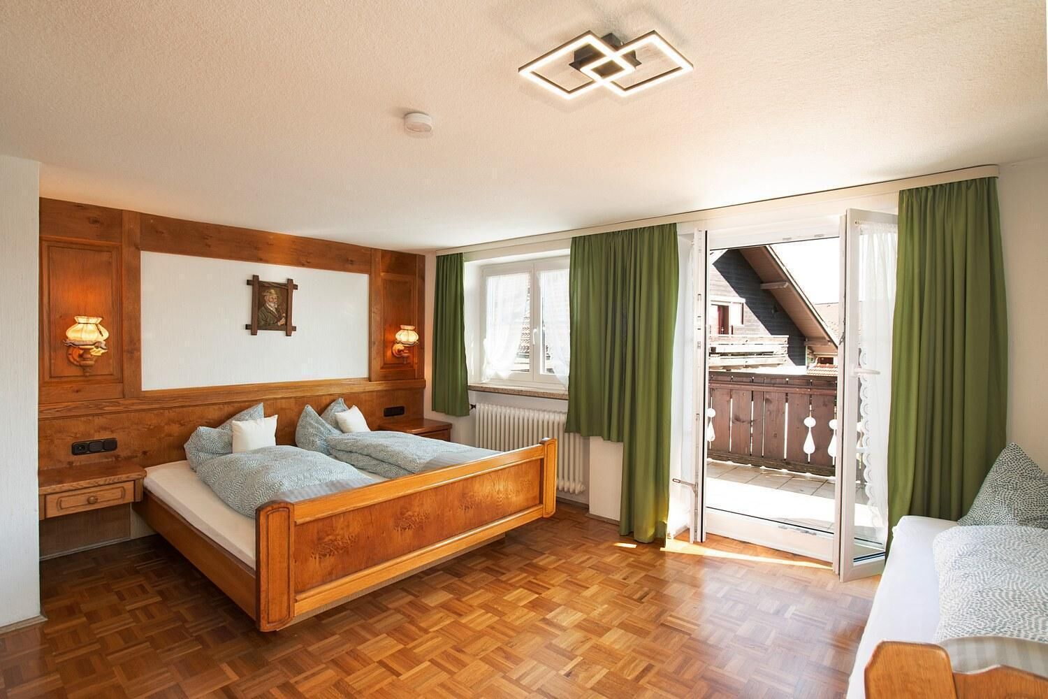 Ein Schlafzimmer mit einem hölzernen Bett, einem Heizkörper, einem Fenster mit Vorhängen und Blick auf einen Balkon.