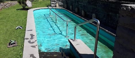 A swimming pool with steps leading into it, surrounded by a stone wall and greenery.
