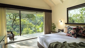 Une chambre avec une grande porte-fenêtre coulissante donnant sur un balcon, un lit agrémenté d’oreillers à motifs floraux et une table de chevet avec une lampe.