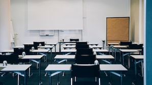 Un aula con filas de escritorios y sillas, una pizarra y una pantalla de proyección.