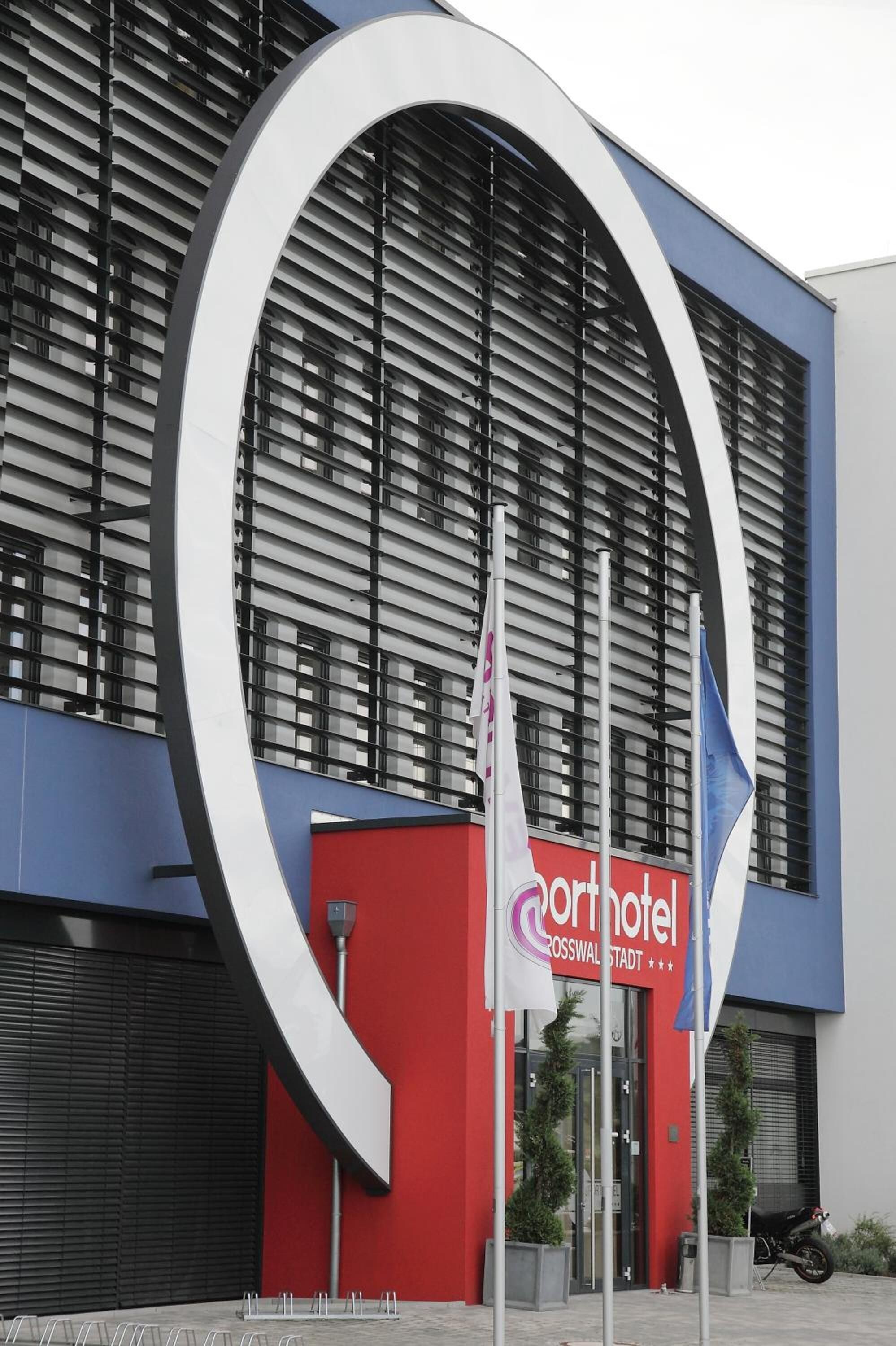 Moderni hotelli, jonka tunnusmerkkejä ovat suuri pyöreä logo, punainen julkisivu ja kyltti, jossa lukee ”Hotel Crosswallstadt”.