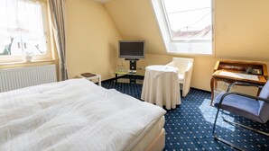 A hotel room with a bed, a desk with a computer, a chair, a TV, and a window with curtains.