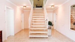 A spacious hallway with a central staircase leading to an upper floor, a potted plant, and a mirrored wall on the right.