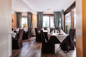 Comedor con mesas dispuestas para cuatro, cortinas oscuras y vistas al exterior.