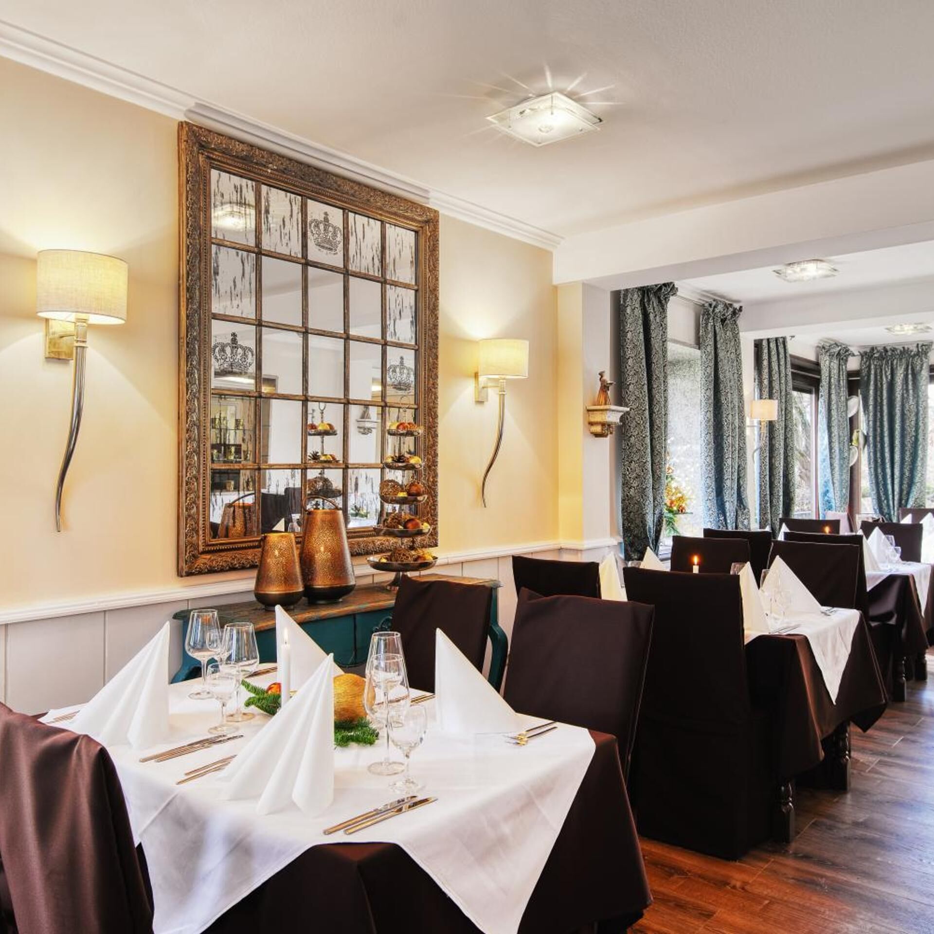 A restaurant with tables set for dining, a large mirror on the wall, and decorative wall sconces.