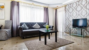 Ein Wohnzimmer mit einer Couch, einem Couchtisch, einem Fernseher auf einem Schrank und gemusterten Vorhängen.
