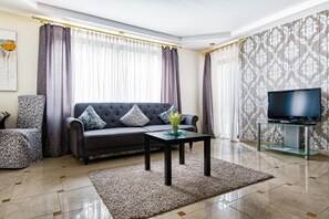 Una sala de estar con un sofá, una mesa de centro, un televisor sobre un mueble bajo y cortinas con estampado.