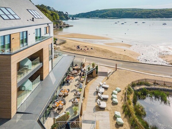 A modern building with a rooftop terrace overlooking a beach and water.