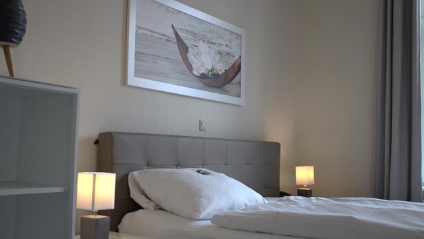 A hotel room with a bed, two bedside lamps, a nightstand, a framed picture on the wall, and a window with curtains. - Hotel & Gastro Adler Gmbh (Itzehoe)