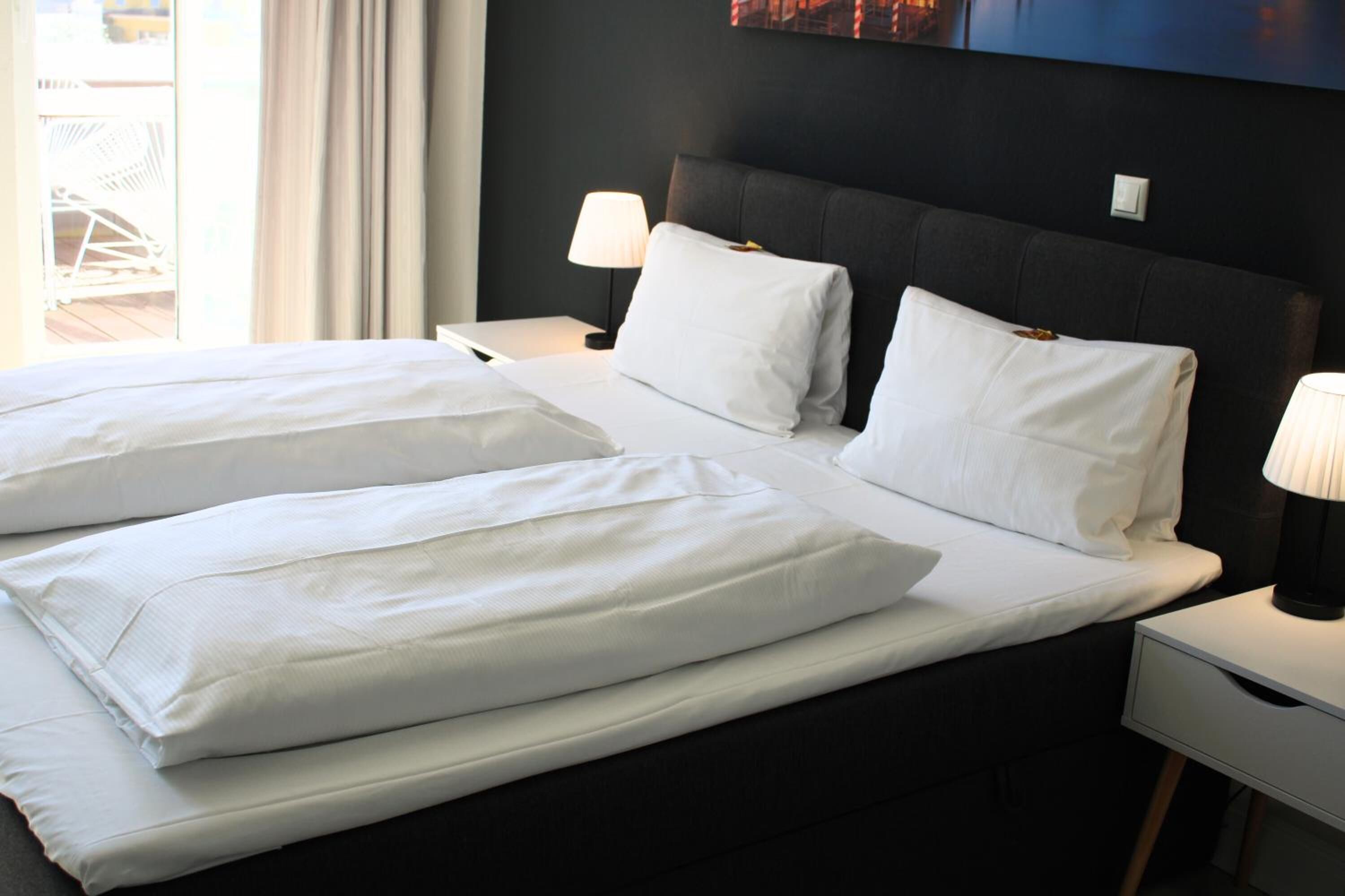 Una habitación de hotel con una cama grande, dos lámparas de noche y un cabecero oscuro.