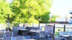 An outdoor patio area with seating arrangements including tables and chairs, a built-in bench, and a fire pit. - Hotel & Gastro Adler Gmbh (Itzehoe)