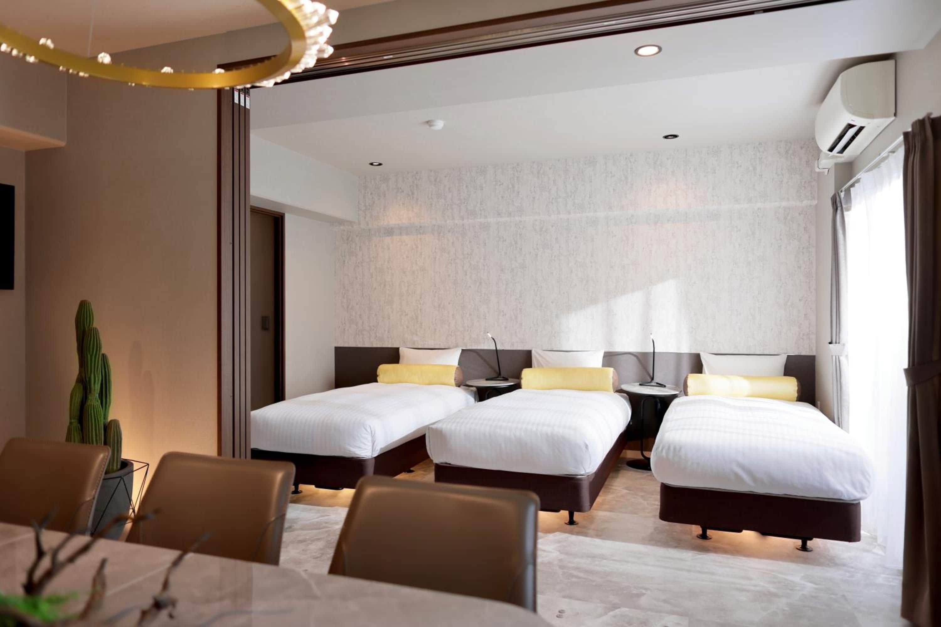 A hotel room with two beds, a dining area, and a large window.