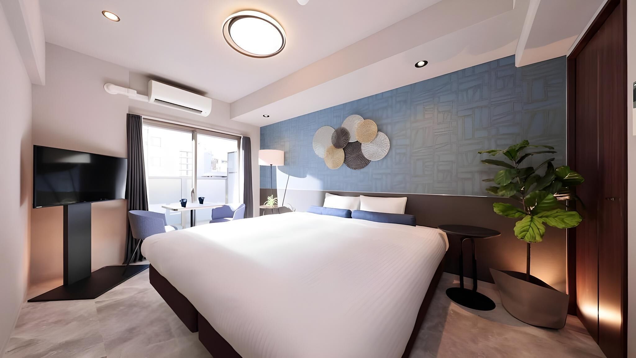 Una habitación de hotel moderna con una cama grande, un televisor de pantalla plana, un escritorio y una planta en maceta.