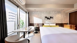Une chambre d’hôtel avec un grand lit, une petite table avec une chaise, un bureau et une fenêtre avec des rideaux.