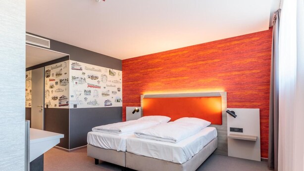 Une chambre d’hôtel moderne avec un lit double, une table de chevet, une petite table et un mur orné d’un motif texturé rouge.
