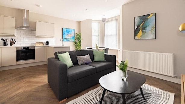 A modern kitchen with white cabinets, a black stove, and a dining area with a black table and a black sofa with green cushions.