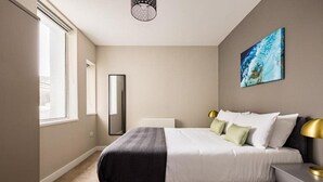 A bedroom with a bed, bedside table, lamp, and a painting on the wall.