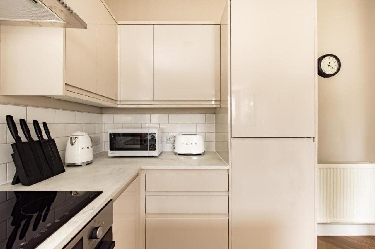 Eine kleine Küche mit weißen Schränken, einer Mikrowelle, einem Toaster und einer Uhr an der Wand.