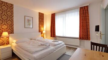 Ein Hotelzimmer mit Doppelbett, zwei Nachttischlampen, einem gerahmten Bild an der Wand und einem Vorhangfenster.