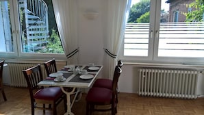 A dining area with a table set for four, two chairs on each side, a radiator below the windows, and a view of a white fence and greenery outside. - Hotel Am Park (Braunschweig)