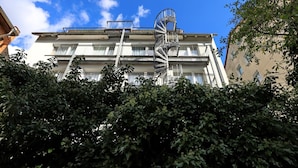 A multi-story building with a spiral staircase, balconies, and dense foliage in the foreground. - Hotel Am Park (Braunschweig)