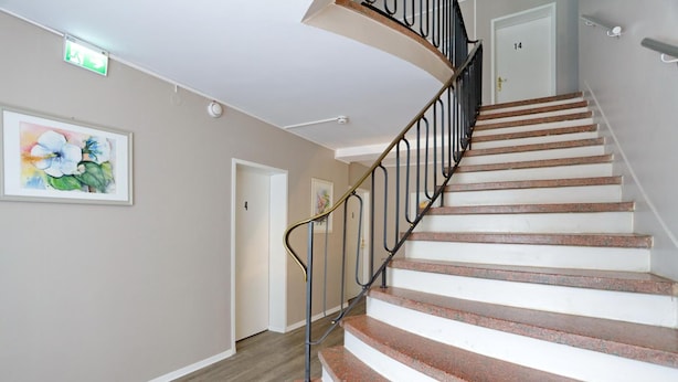 A spiral staircase with a metal railing, beige walls, and a wooden floor. - Hotel Am Park (Braunschweig)