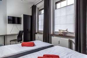 A hotel room with two beds, a desk, a chair, a TV, and a window with blinds. - Aparthotel Menden (Menden)