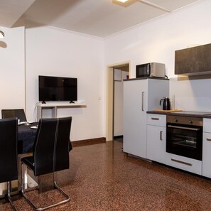 A compact kitchen with a TV, microwave, oven, and a dining area with chairs. - Aparthotel Menden (Menden)