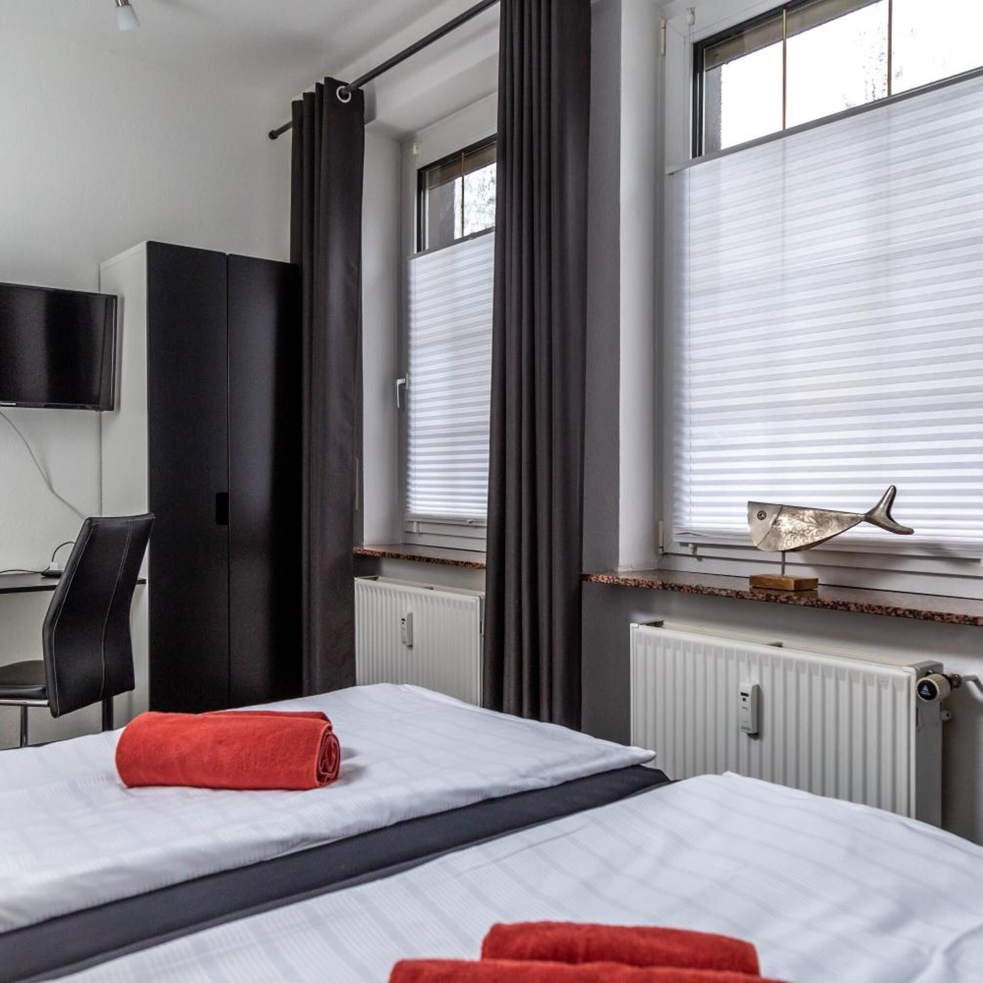 A hotel room with two beds, a desk, a chair, a TV, and a window with blinds.