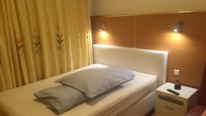 Una cama bien hecha con un almohadón, una mesita de noche con un control remoto y una lámpara de pared.
