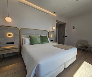 A modern hotel room with a large bed, bedside tables, a chair, and a desk. - Malaga Vibes (Málaga)