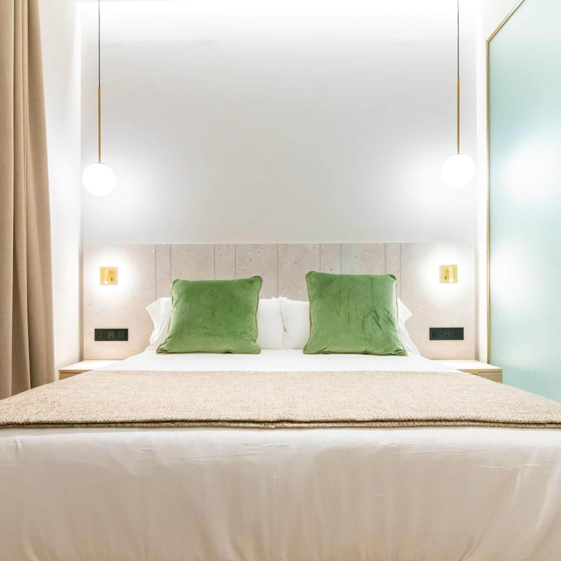 Habitación de hotel moderna con una cama grande, dos almohadas verdes y un cabecero de madera.