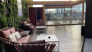 Una zona esterna moderna con mobili in vimini e una parete vetrata che offre vista sulla città.