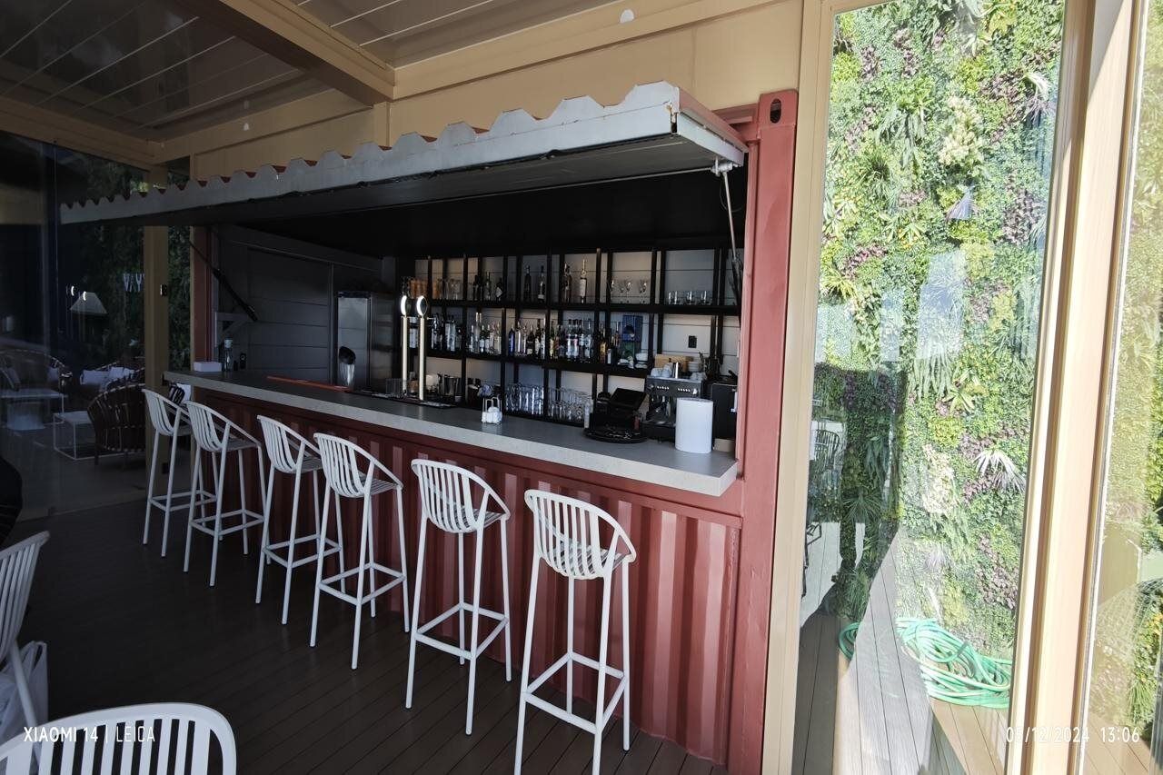 Zona de bar con taburetes blancos y una estantería llena de botellas.