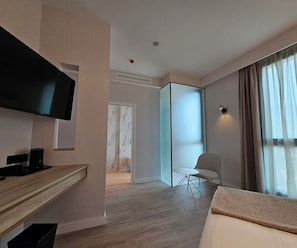 A hotel room with a flat-screen TV, a desk with a chair, a bed, a window with curtains, and a sliding door leading to another room. - Malaga Vibes (Málaga)